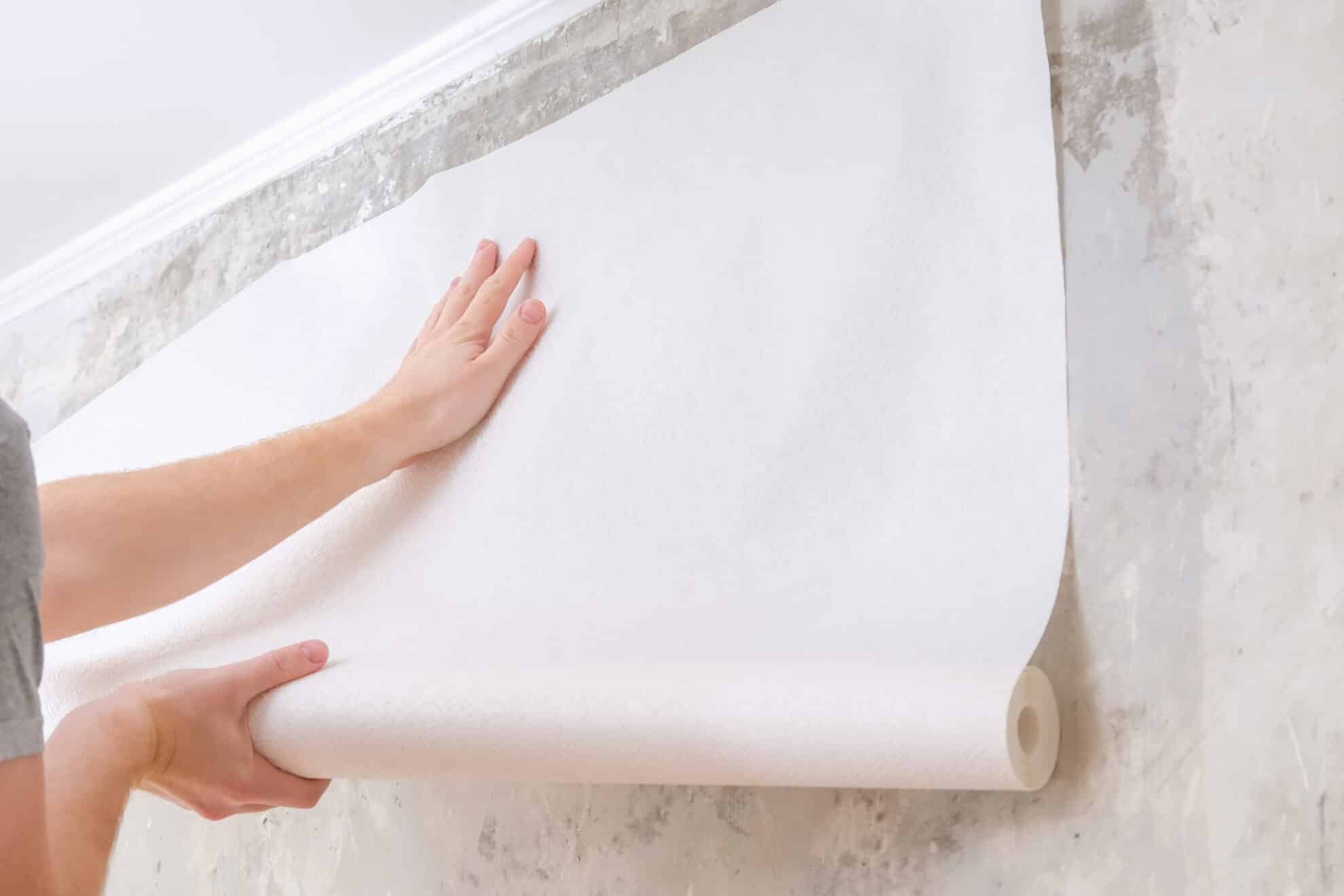 A man rolls out a roll of white wallpaper on the wall with glue. Wallpapering. Repair of a room, apartment, house.
